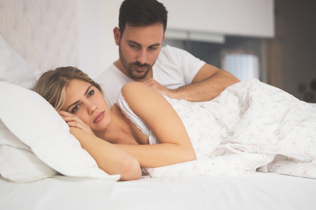femeie trista in pat care sta departe de partenerul sau
