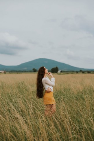 femeie care gandeste intr-un lan de grau cu muntii in spate