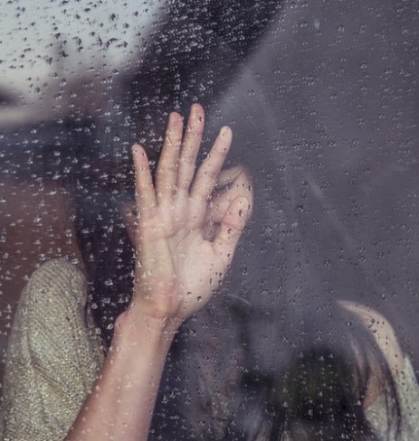 femeie care plange si tine mainile pe un geam acoperit de ploaie