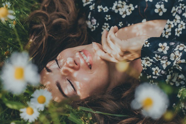 femeie care zambeste dintr-un camp plin cu flori