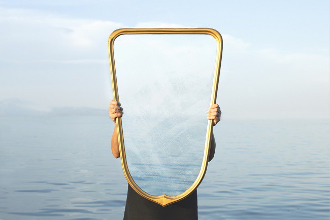 femeie care tine in mana o oglinda inversa ce reflecta apa