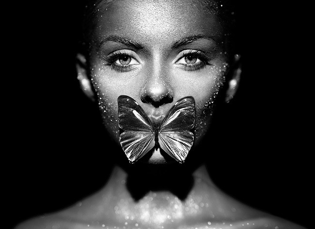 femeie ganditoare pe un fundal negru cu un fluture pe gura