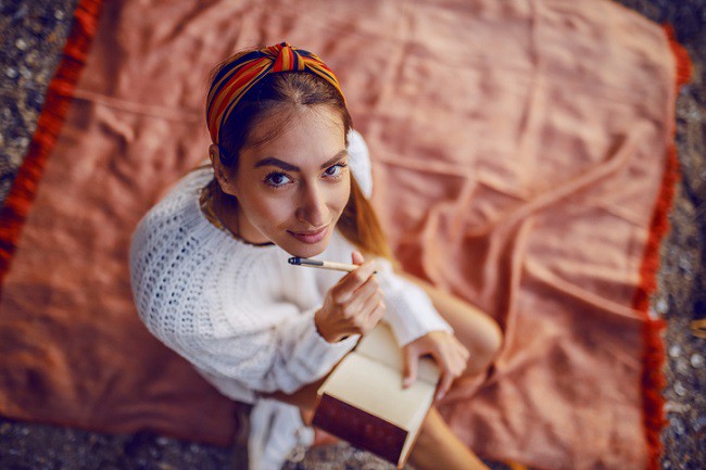 imagine cu fata care se relaxeaza scriind in jurnal pe o patura