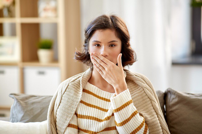 femeie bolnava cu bluza in dungi care tine mana la gura