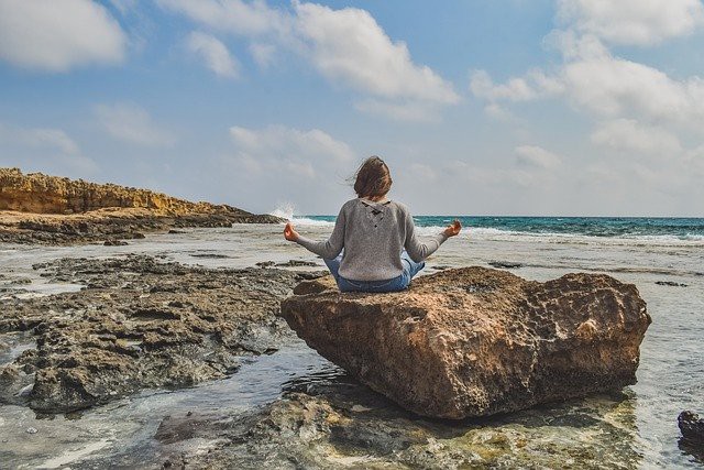 femeie care mediteaza cu spatele pe pietre pe un rau