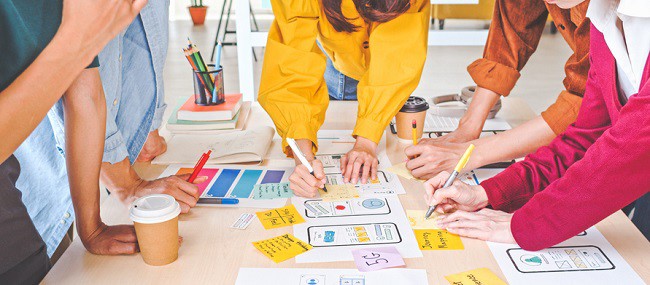 colegi asezati in jurul unei mese care lucreaza la un proiect, grup vesel si colorat