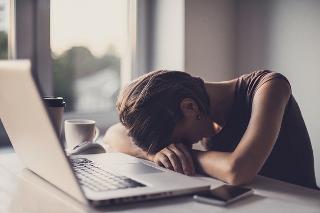 femeie obosita care sta cu capul pe un birou cu laptop si cafea