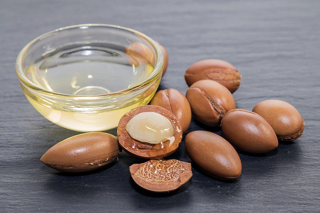 bol de sticla cu ulei de argan alaturi de fructe de argan