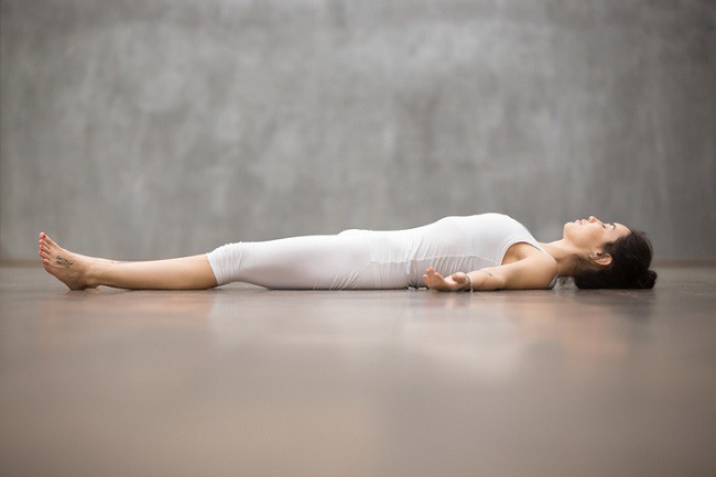 femeie in echipament alb de yoga intinsa pe podea in pozitia Shavasana