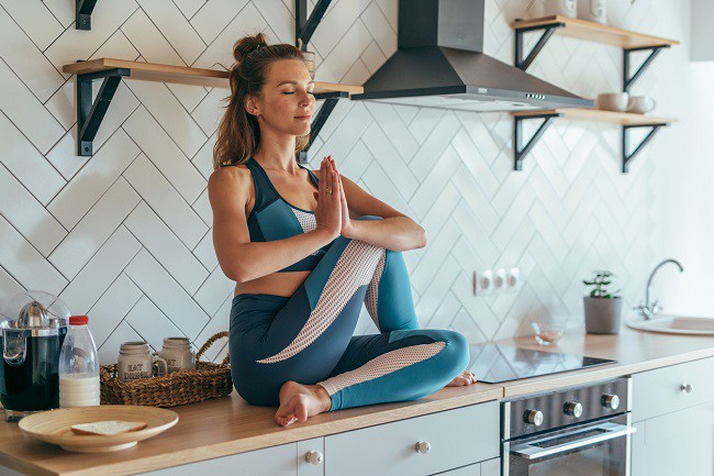 femeie care se relaxeaza facand yoga pe blatul din bucatarie