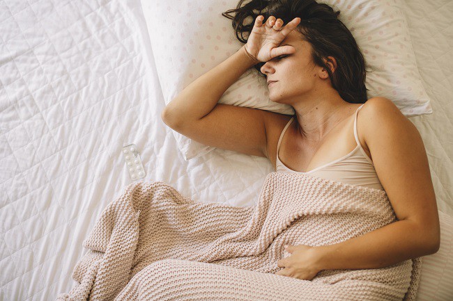 femeie care sta pe pat intinsa cu durere de cap si de stomac
