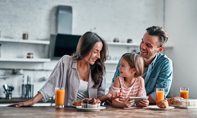 familie cu parinti si copil care stau la masa si beau suc de portocale