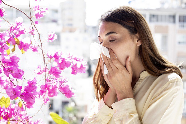 femeie care stranuta din cauza alergiei la polen langa flori roz