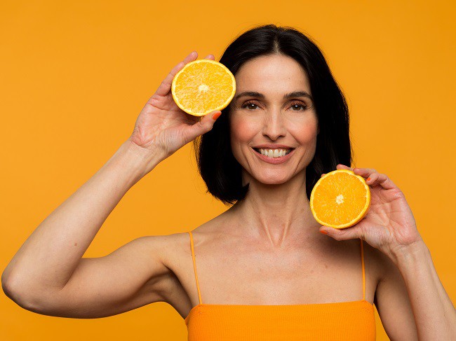 femeie frumoasa imbracata in portocaliu care tine doua portocale in mana