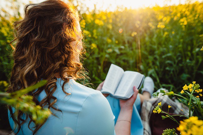 fata care sta intr-un camp de floarea soarelui si citeste rugaciuni dintr-o carte