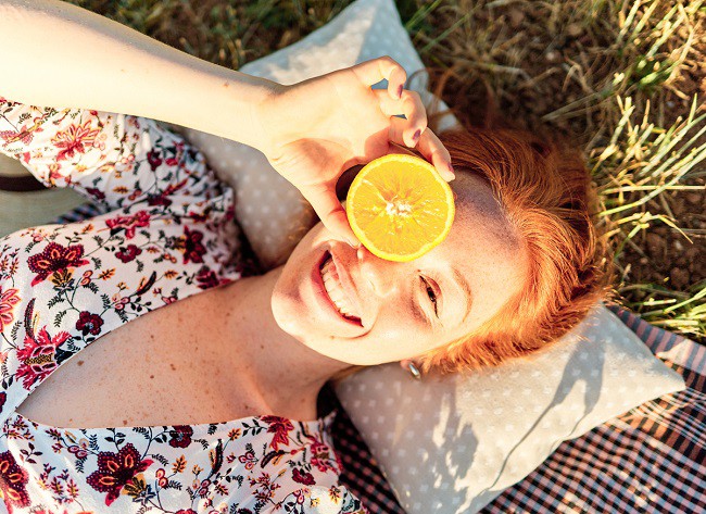 femeie roscata fericita aflata la picnic care tine o lamaie pe fata
