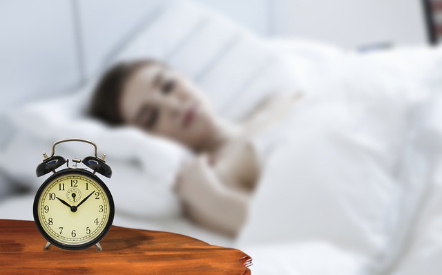 femeie in pat care priveste alarmata la ceasul ce arata ora 10 