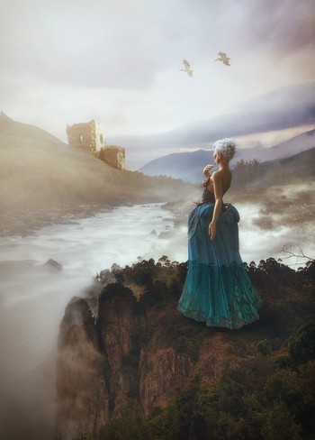 fata blonda imbracata in rochie albastra care priveste in zare la un castel cu pasari pe cer