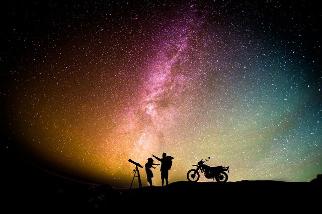 cuplu care se uita la cer cu telescopul alaturi de o motocicleta