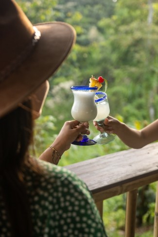 femei care ciocnesc un pahar de Piña Colada pe balcon in vacanta