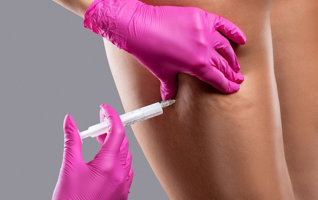femeie careia un medic cu manusi roz ii face injectie in coapsa