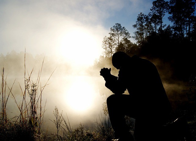 barbat care se roaga pe fundalul cerului aprins, in genunchi si inconjurat de ceata