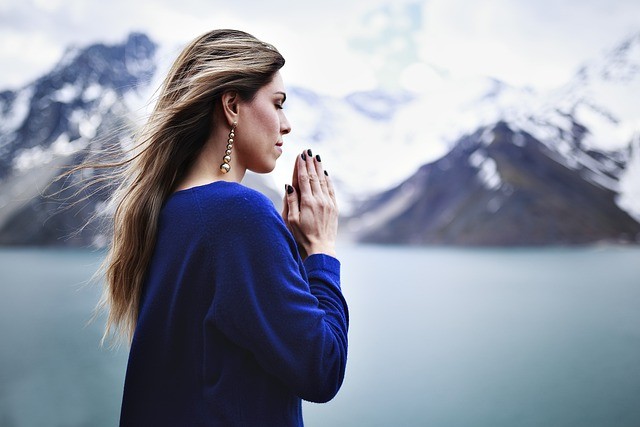 femeie frumoasa imbracata in albastru care se roaga pe un fundal cu munti si lacuri
