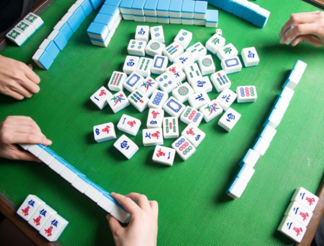 masa verde cu piese de mahjong si jucatori care pun pe tabla