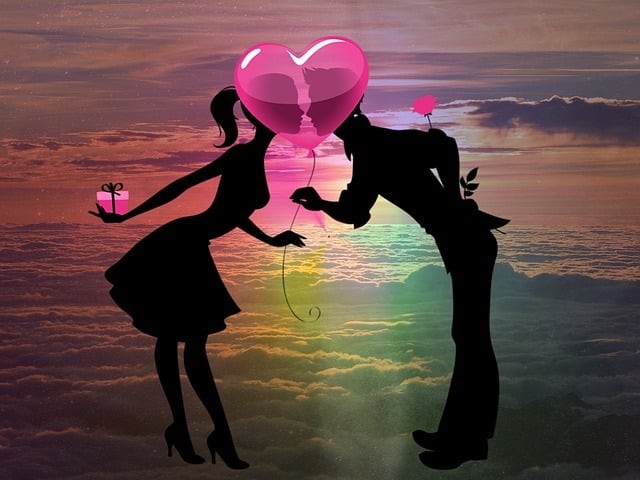 fata si baiat ibdragostiti care se apleasa sa se sarute in spatele unei inimi roz pe fundalul unei ape si al cerului