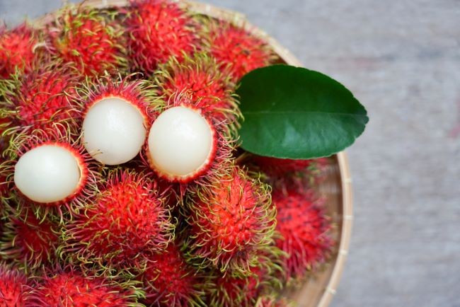 prim plan cu bol in care se afla fructe de rambutan decojite si fruncte de ramburan intregi cu tepi rosii
