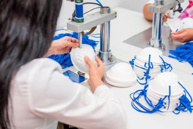 femeie imbracata intr-un halat care sta intr-un laborator si creeaza masti la microscop