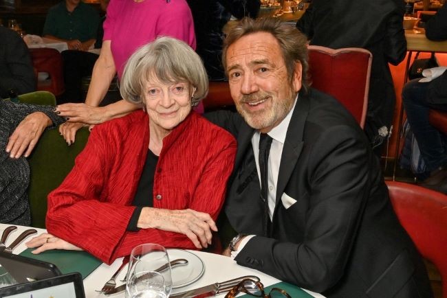 imagine cu maggie smith in sacou rosu si un barbat cu barba in costum