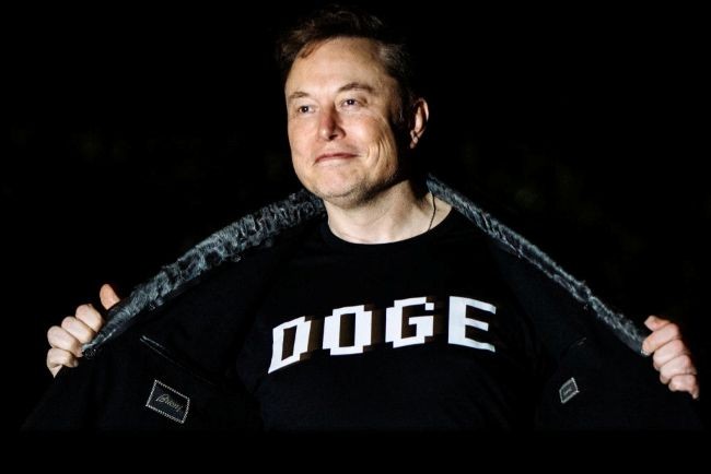 elon musk poarta un tricou pe care scrie DOGE si un cardigan