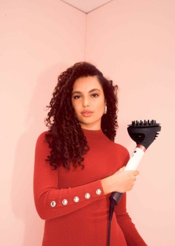 fata care tine in mana un aparat de coafare de la dyson si e imbracata in rochie rosie