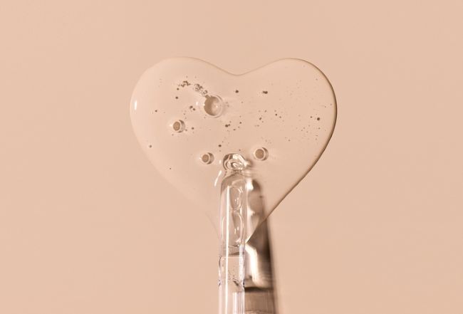 detaliu cu un flacon cu cosmetice din care e picurata substanta pe un fundal roz