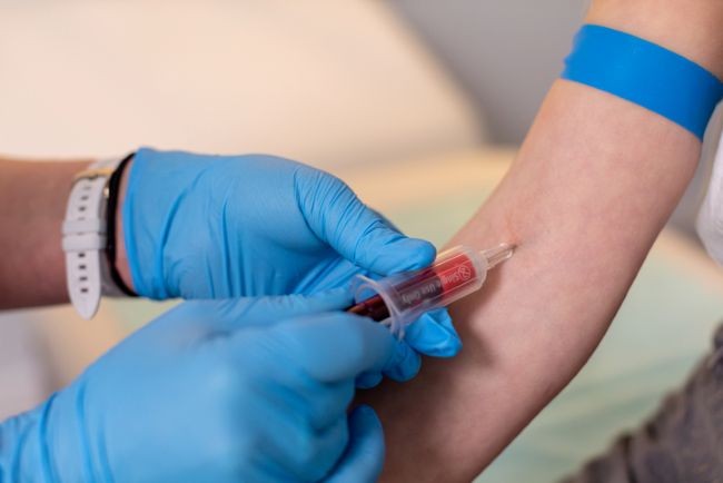 doctor care poarta manusi albastre si injecteaza un ser in bratul unei femei