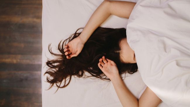 femeie cu par lung si negru care doarme in pat acoperita ci patura in pat