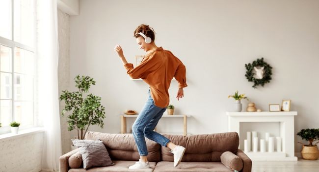 femeie imbracata in portocaliu care sare fericita pe o canapea