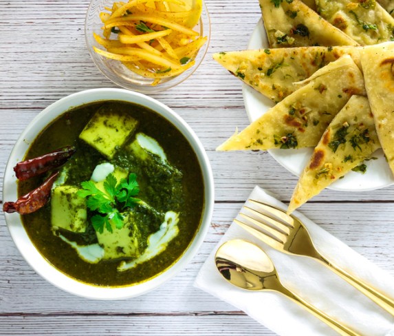 bol cu saag paneer alaturi de recipient cu cartofi prajiti si paine naan