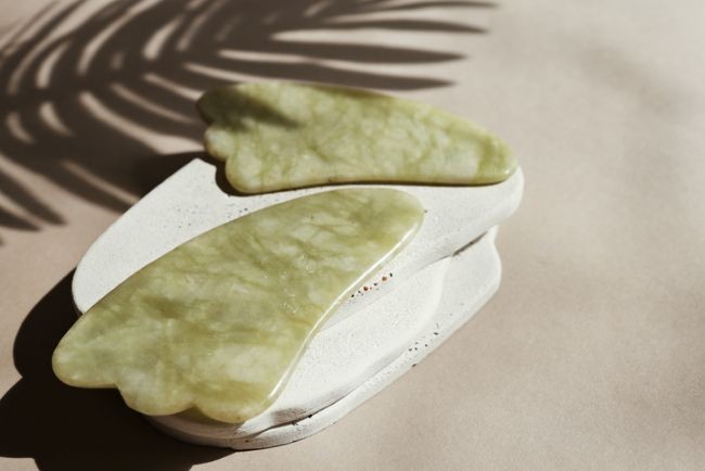 imagine cu pietre gua sha pe un blat de marmura cu o planta in apropiere