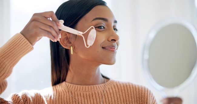 fata de culoare care isi face masaj facial cu roller facial in oglinda