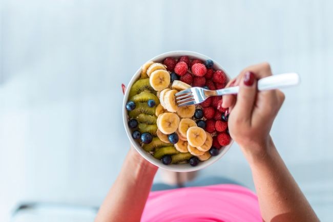 femeie cu bol cu fructe in mana cu fructe de padure, banane si kiwi