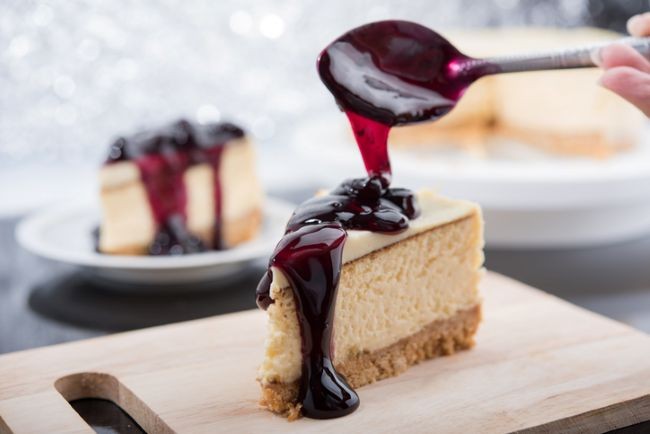 felie de cheesecake in prim plan pe un platou de lemn cu alte deserturi in background