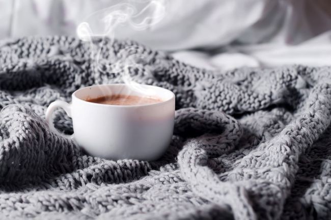 imagine cu ceasca alba cu ceai de cacao pe o patura de lana gri inchis