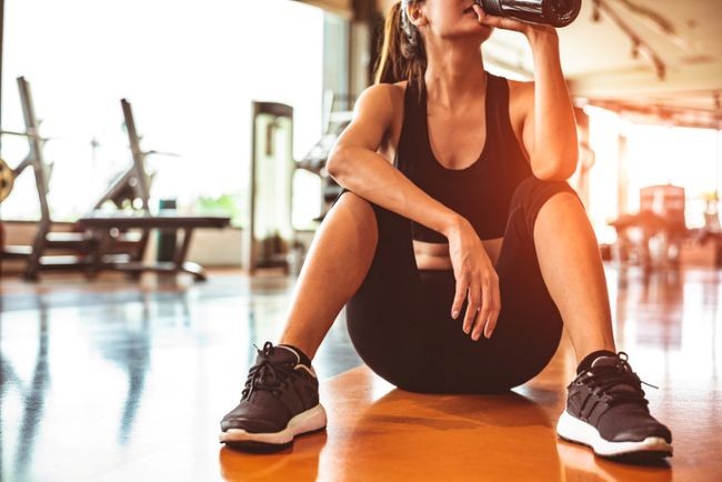 fata la sala pe saltea obosita care bea apa in costum de sport