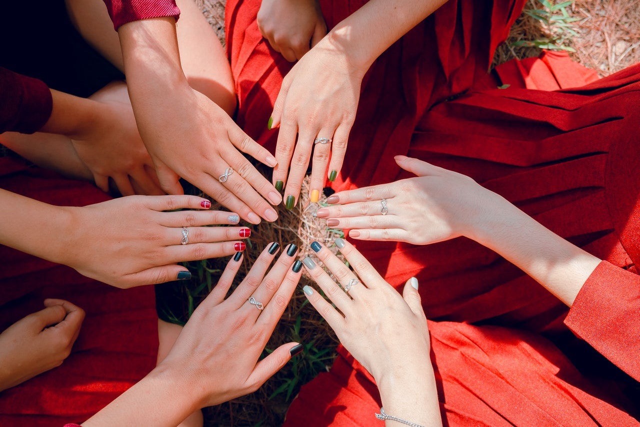 femei cu unghii colorate asezate cu mainile in cerc