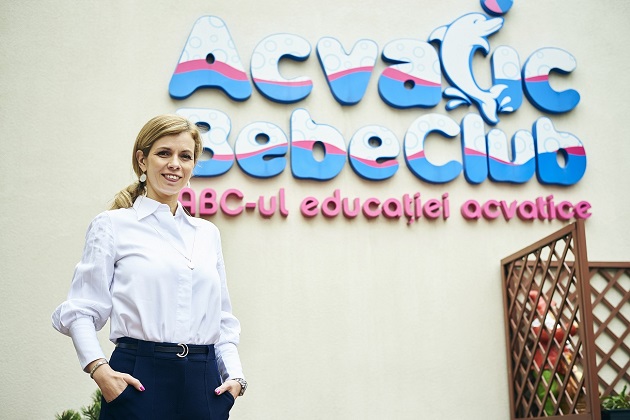 Femeie care pozeaza in fata logo-ului Acvativ Bebe Club