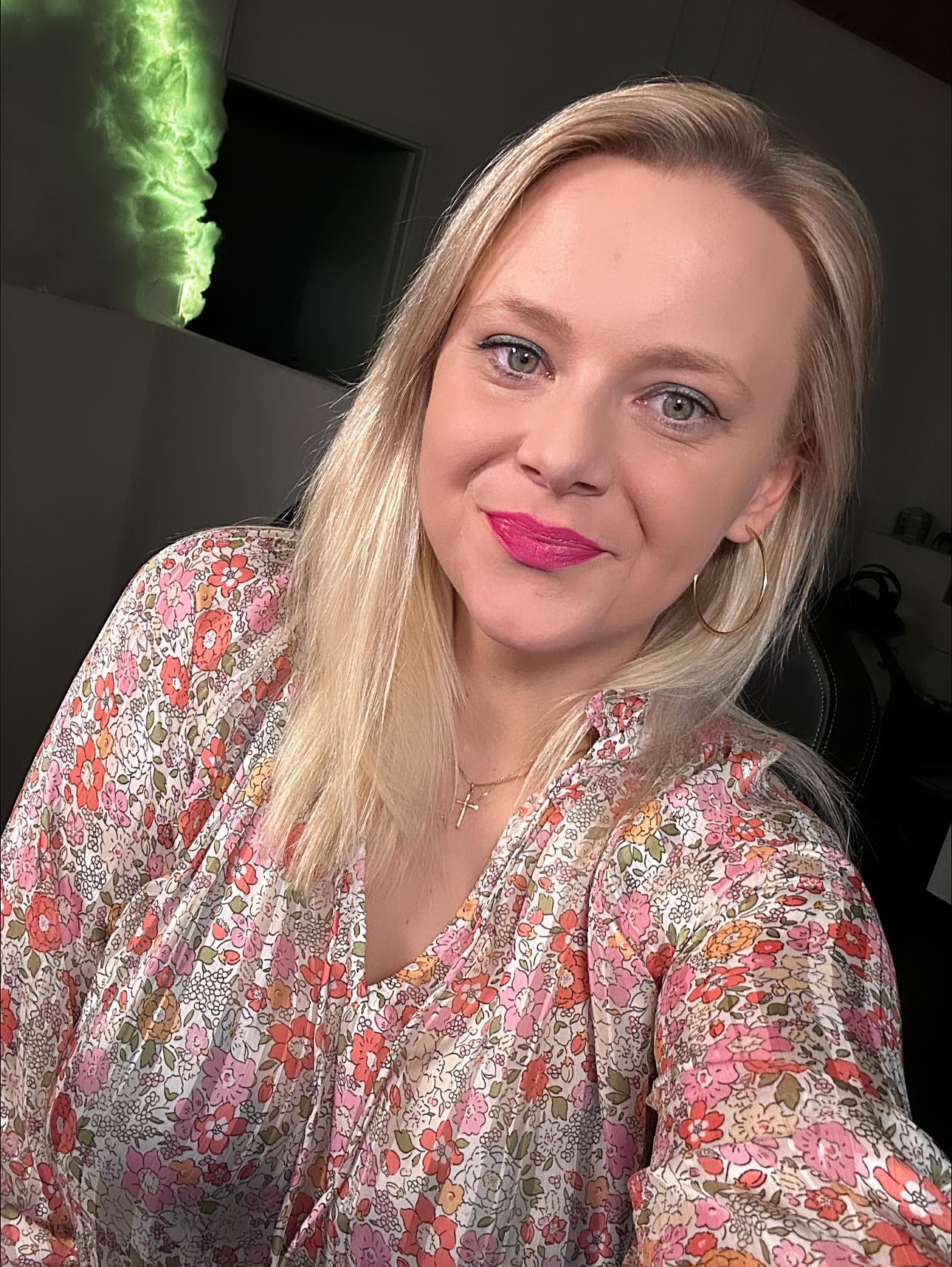 o femeie blonda imbracata intr-o bluza cu imprimeu floral zambeste spre camera