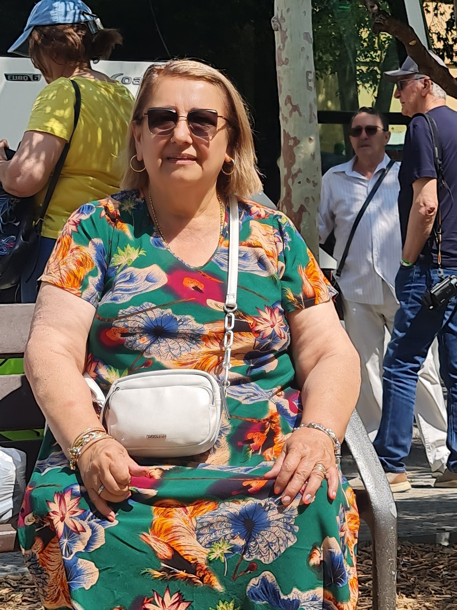 femeie imbracata intr-o rochie cu imprimeu floral cu ochelari de soare la ochi, sta pe un scaun