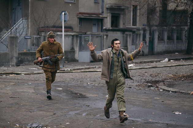 imaginea unui soldat din armata urmarind un barbat civil cu mainile ridicate in aer